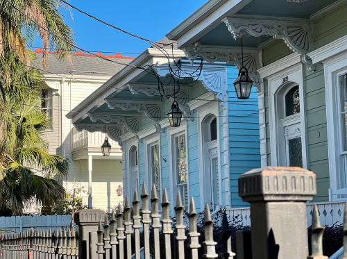 Historic New Orleans homes with ornate decorative trim, hanging lanterns, raised porches, and iron fencing lining a residential street.