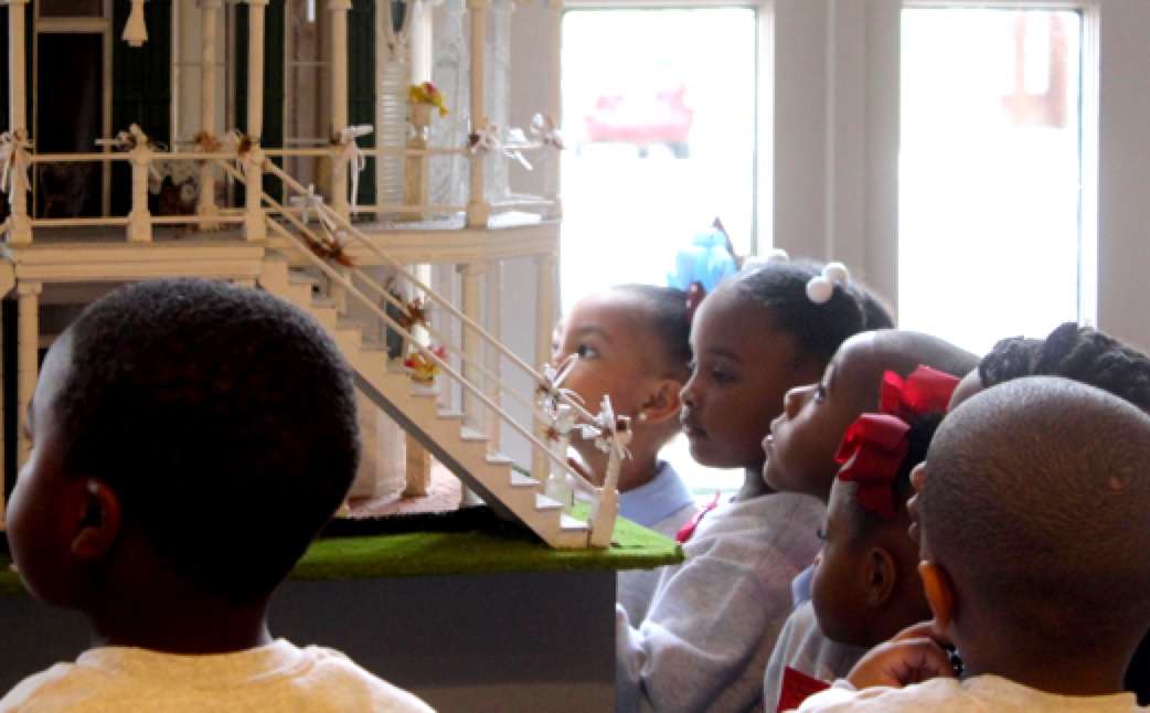 A group of young children look closely at a detailed architectural model of a historic building.