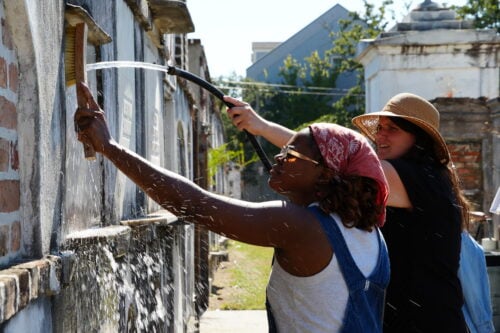 Two woman cleaning and restoring a historic tomb in St. Louis Cemetery no. 2.