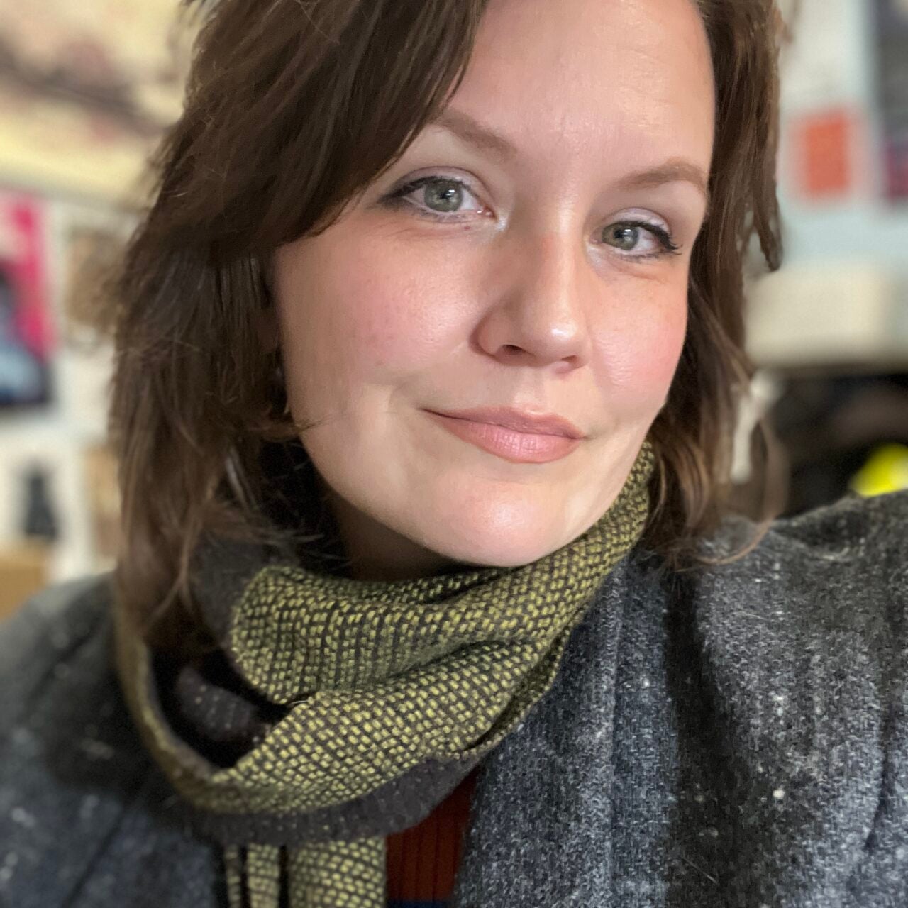 Amanda Fallis, smiling in a close-up portrait while wearing a dark gray sweater and patterned green scarf.