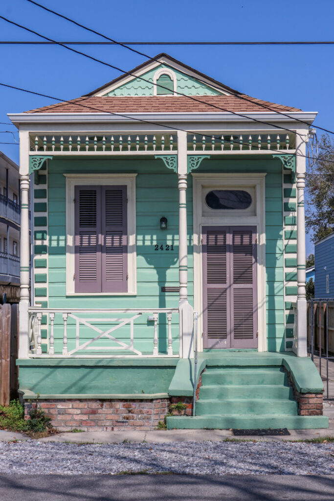 Front Facade of a 2-bay teal and purple eastlake style shotgun home.