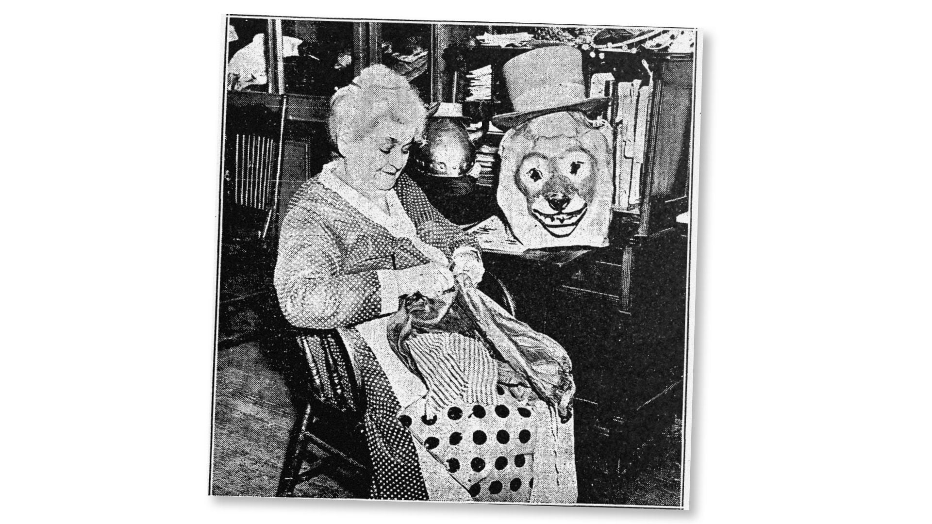 Julia Segui Alabau sits in a chair knitting, with a large pig puppet beside her in a shop filled with textiles and furnishings.