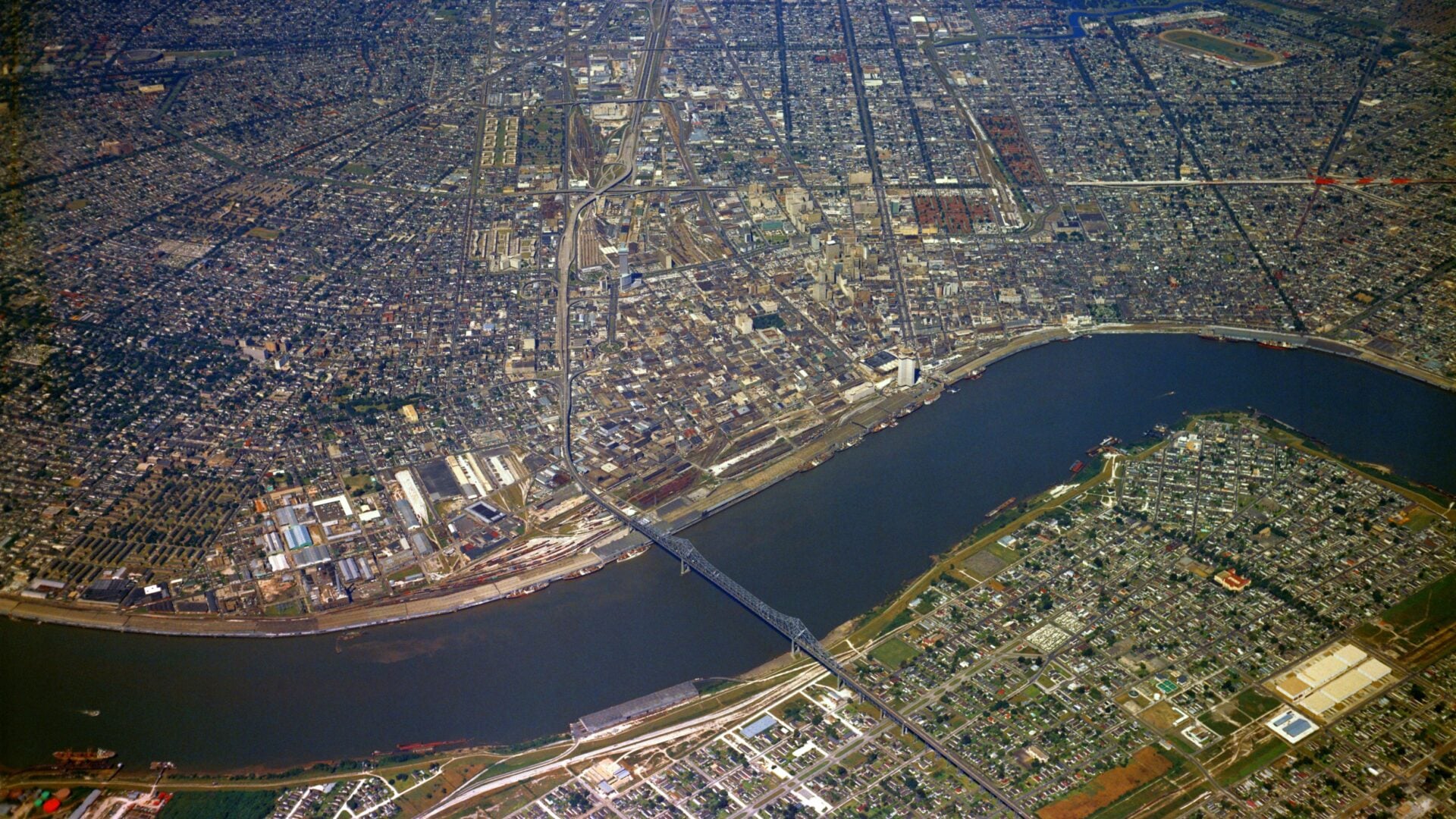 Historic aerial photograph of New Orleans showing the Mississippi River, downtown skyline, the Crescent City Connection, port facilities, and surrounding neighborhoods viewed from above.
