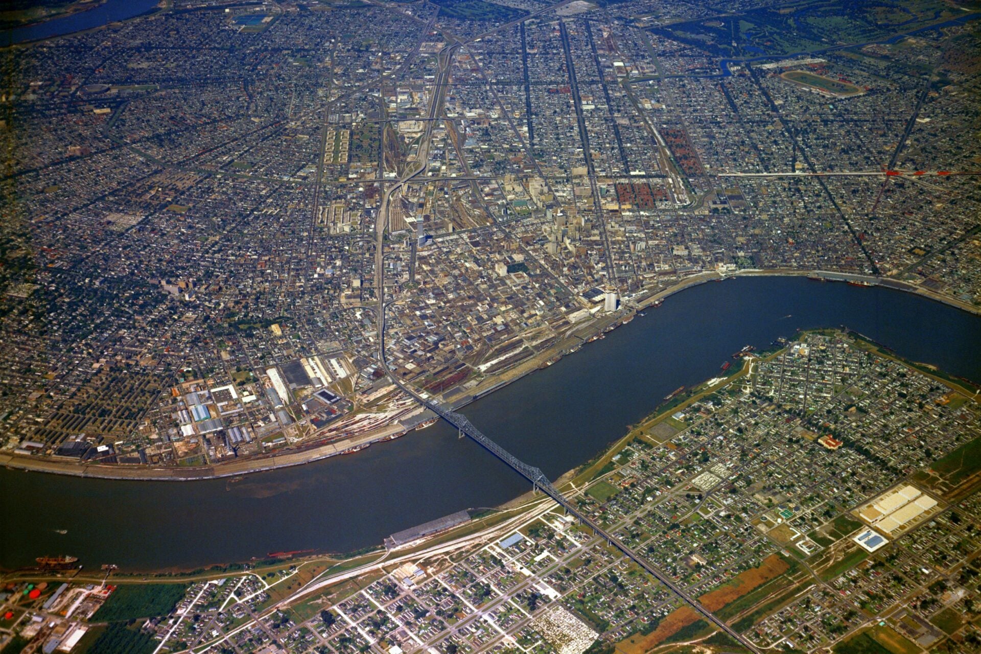 Historic aerial photograph of New Orleans showing the Mississippi River, downtown skyline, the Crescent City Connection, port facilities, and surrounding neighborhoods viewed from above.
