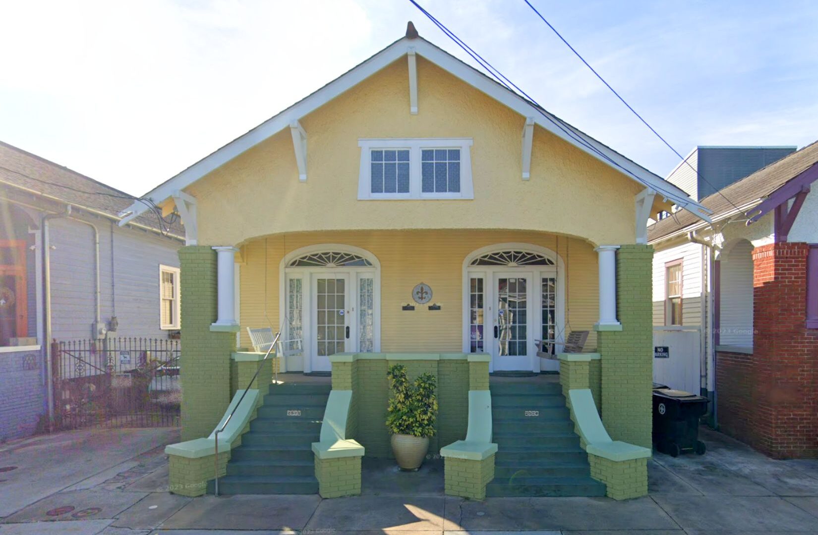 Historic double shotgun house at 2522 Chartres St. in New Orleans, featuring a pale yellow facade, green brick porch columns and steps, decorative arched doorways, and a front porch.