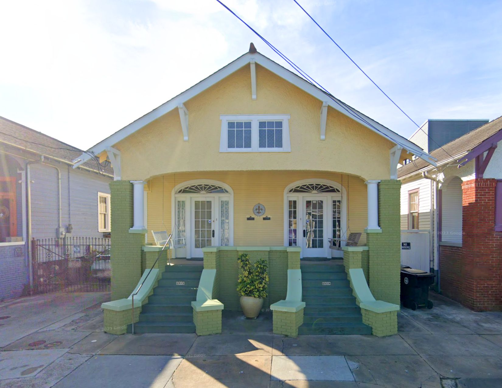 Historic double shotgun house at 2522 Chartres St. in New Orleans, featuring a pale yellow facade, green brick porch columns and steps, decorative arched doorways, and a front porch.