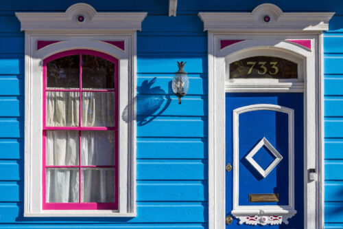Bright blue historic New Orleans home with white trim, a vivid pink window frame, decorative molding, and a blue door numbered 733.