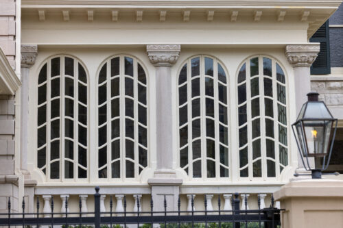 Historic building façade with four tall arched windows featuring intricate wavy muntin patterns, decorative columns and molding, and a black iron fence. Photo by Chris Granger.