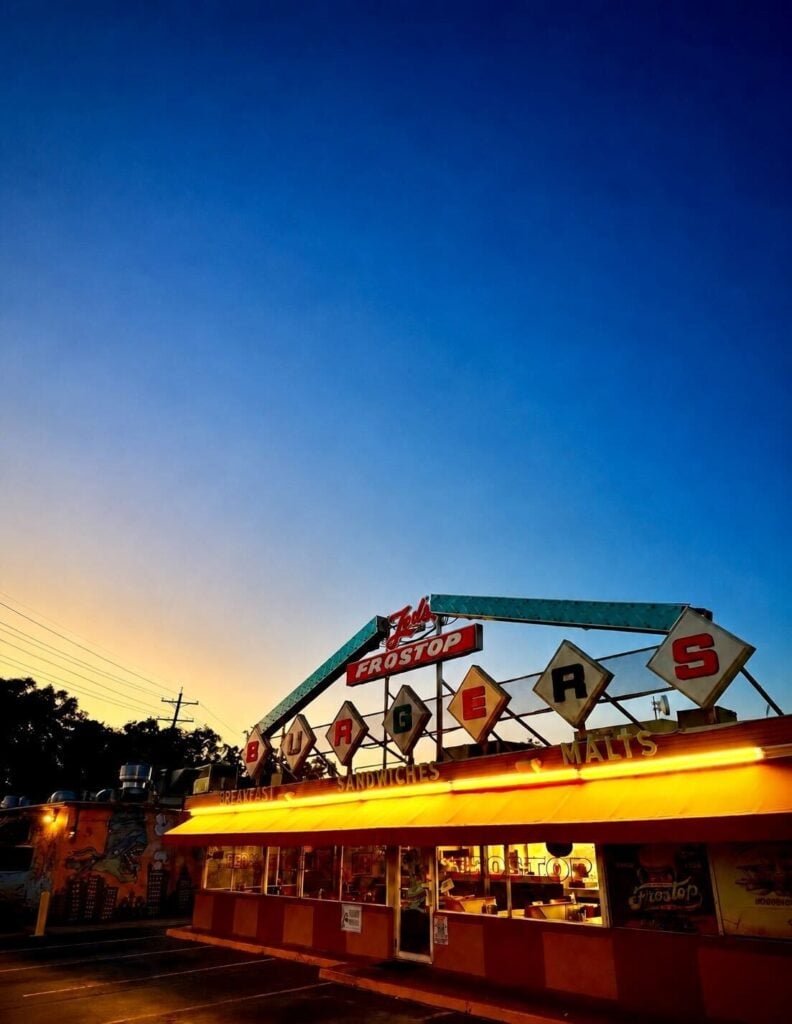 Ted’s Frostop restaurant at dusk, with a vintage rooftop sign, glowing neon lights and a colorful retro storefront.