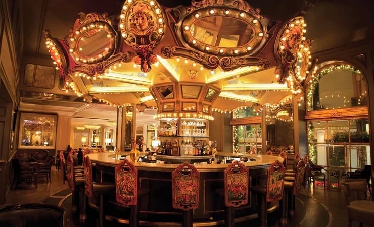 The Carousel Bar at Hotel Monteleone in New Orleans, featuring an ornate, rotating carousel-themed bar with illuminated mirrors, decorative details, and colorful upholstered bar stools.
