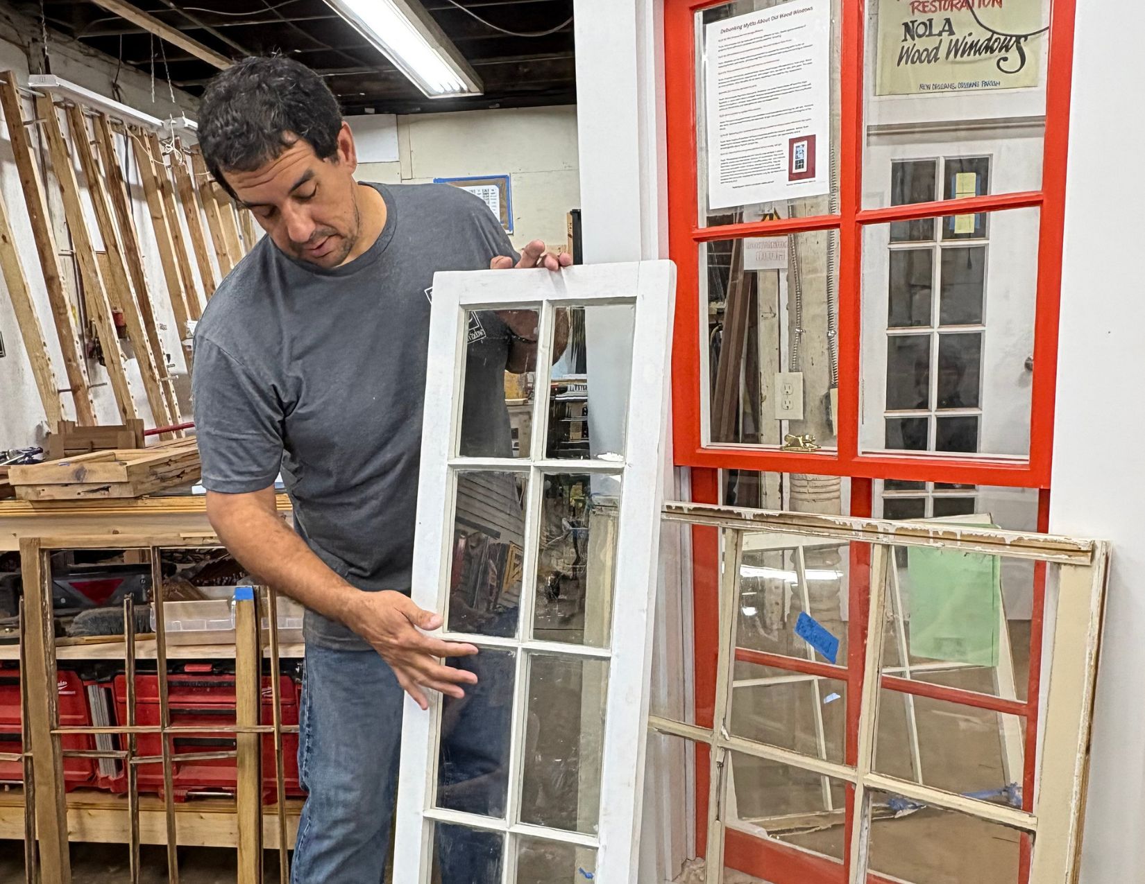 A craftsman demonstrates historic window restoration while holding a restored wood-framed window in a New Orleans woodworking workshop.