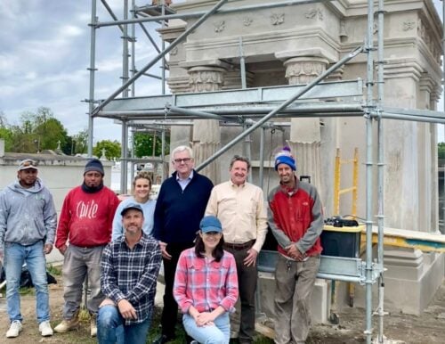 Conservation crew members pose with restorers Dennis Alonzo and Nathan Chapman in front of a historic cemetery tomb undergoing restoration, surrounded by scaffolding.