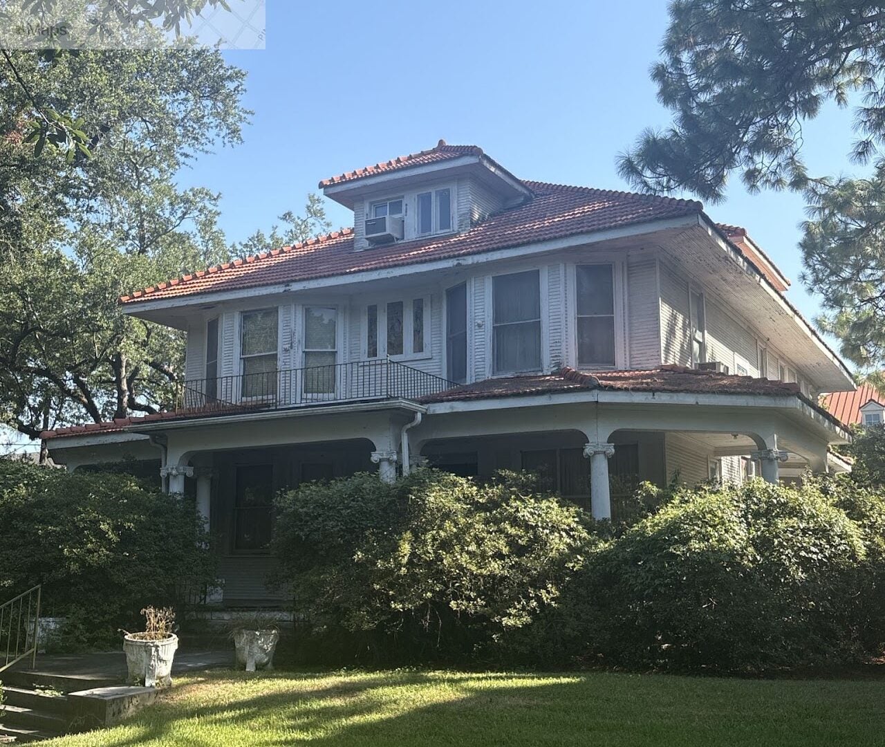 8133 Spruce Street, a historic two-story residence with a red tile roof, white siding, covered front porch, and second-story balcony, surrounded by mature trees and a landscaped lawn.