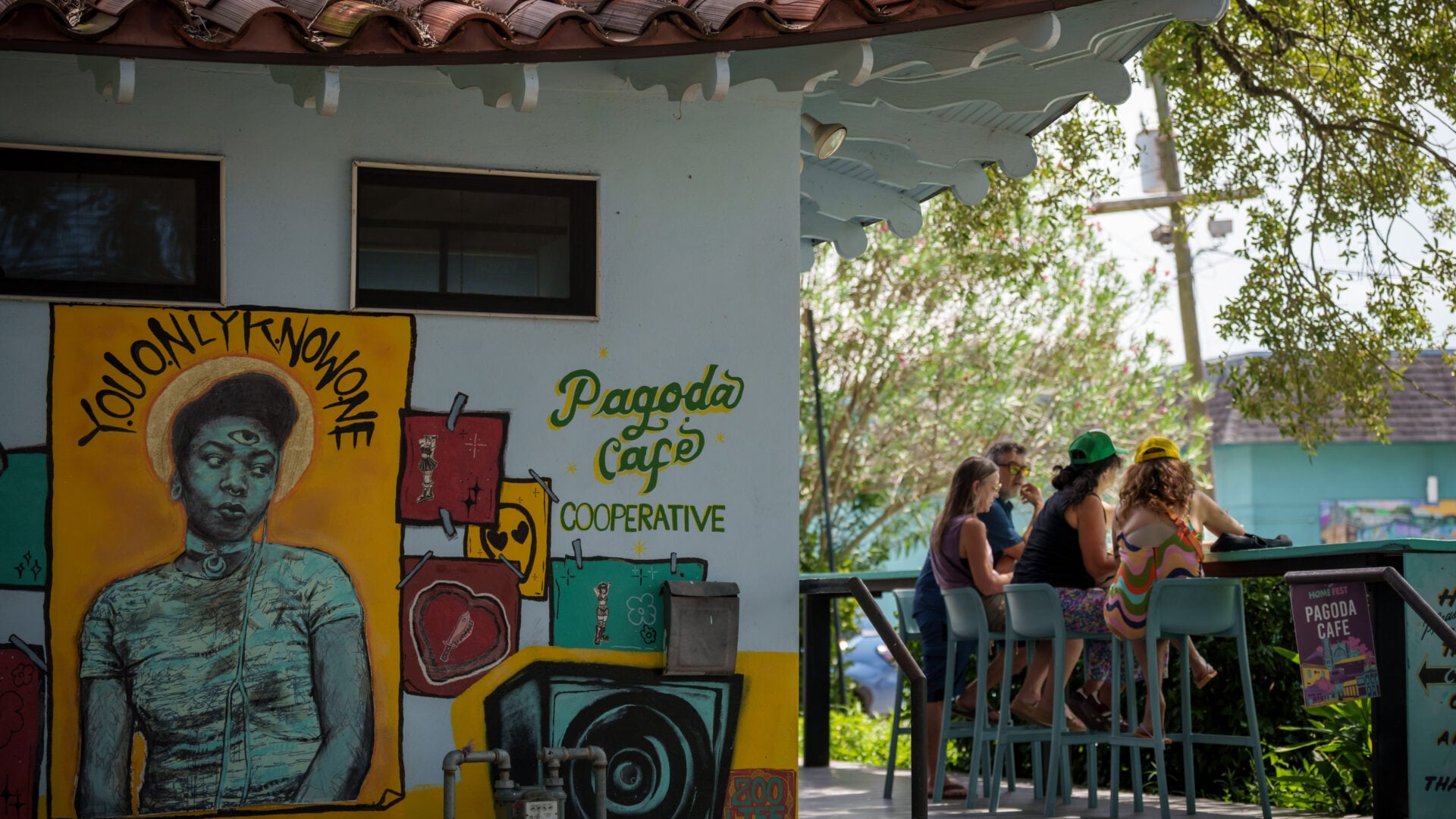 Pagoda Cafe on Bayou Road in New Orleans, featuring colorful exterior murals, including a portrait mural, and a shaded outdoor deck where patrons gather.