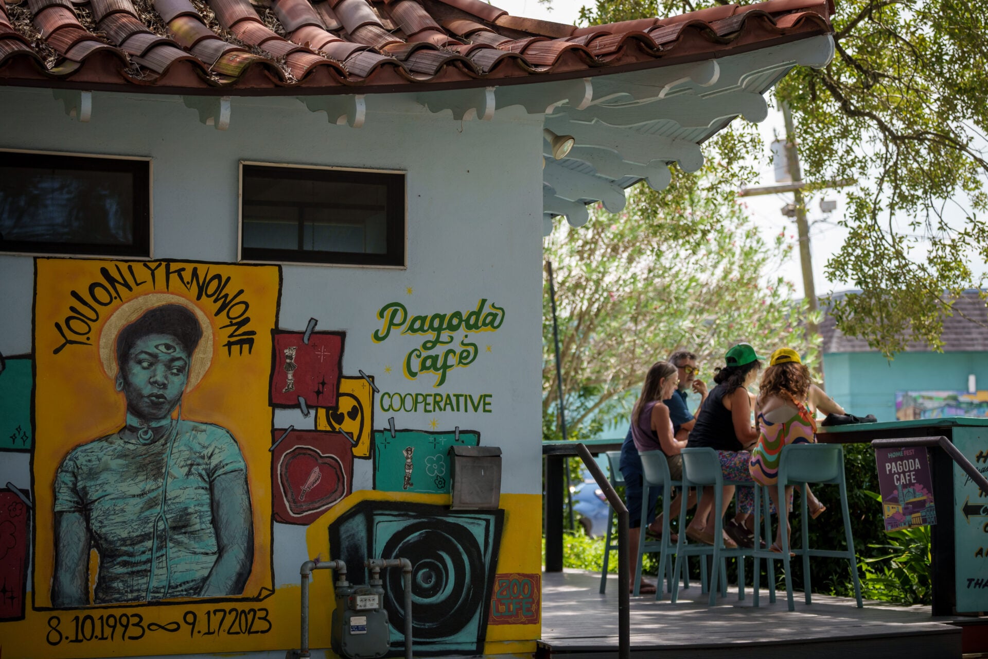 Pagoda Cafe on Bayou Road in New Orleans, featuring colorful exterior murals, including a portrait mural, and a shaded outdoor deck where patrons gather.