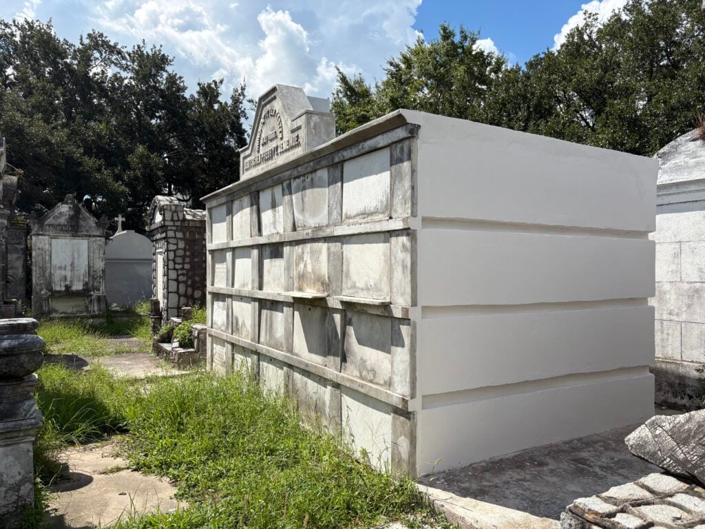 Side view of the German Presbyterian tomb in Lafayette Cemetery No. 1, showing newly restored white stucco along one side contrasted with the weathered marble burial panels on the front.