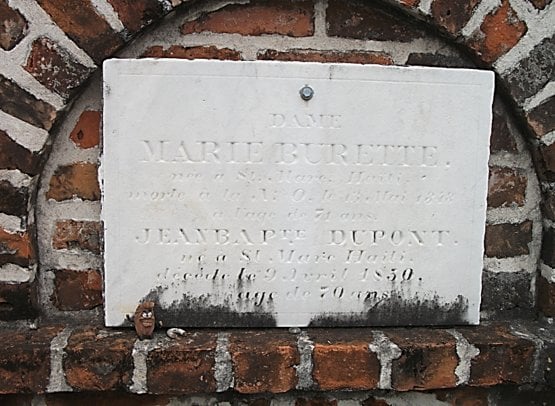 Close-up of a marble tomb inscription for Marie Burette and Jean Baptiste Dupont, set into a red brick wall vault.